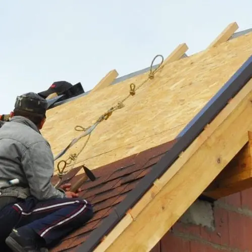 Roofing Construction and Building New Brick House with Modular Chimney, Skylights, Attic, Dormers and Eaves Exterior. Roofers Install, Repair Asphalt Shingles or Bitumen Tiles on the Rooftop Outdoor.