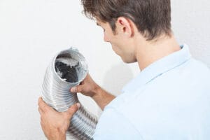Man cleaning dryer vent in home. - Emerson Pro Services
