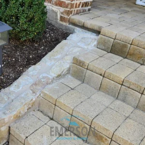 Multi-level concrete paver steps with a mortared natural stone border beside a brick building.